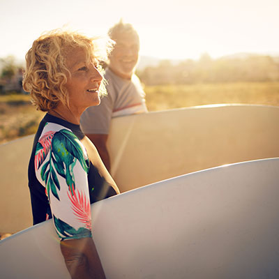 Mature couple on the beach holding surfboards